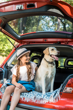 adorable kid sitting with dog on car trunk