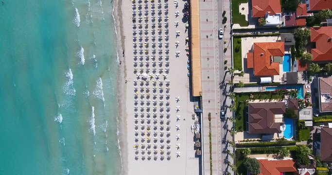 Aerial - Umbrellas on the beach. Top down view of waves hitting sandy shore