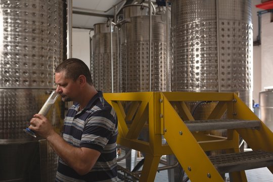 Male worker checking quality of gin in measuring cylinder