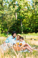 parents and son sitting on blanket at picnic and hugging dog