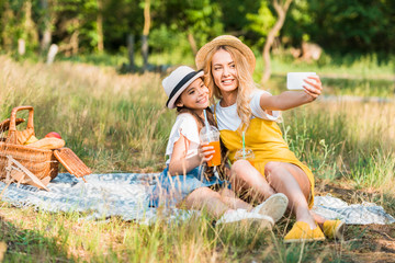 happy mother and daughter taking selfie with smartphone at picnic