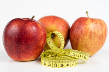 Red apples and a measure of tailor on a white table. Ripe fruits and a tailor's centimeter.
