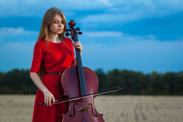 Professional female cello player in red dress with instrument outdoors