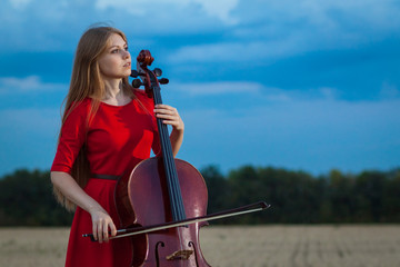 Beautiful woman professional musician in red dress with cello outdoors © Andrey Milkin