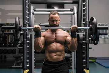 Fototapeta na wymiar Hombre fuerte con grandes músculos levantando peso mientras entrena en el gimnasio. Ponerse en forma