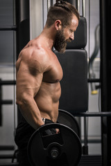 Fototapeta na wymiar Hombre fuerte con grandes músculos levantando peso mientras entrena en el gimnasio. Ponerse en forma