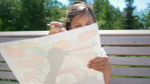 Little girl painter draws with a brush sitting on the bench in the park