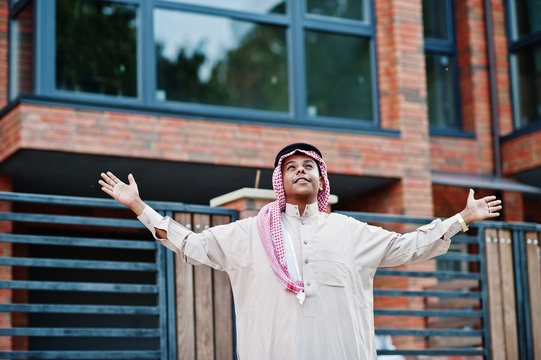 Middle Eastern arab man posed on street against modern building up his hands in the air, looking at the sky and pray.