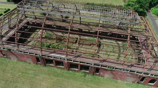 Aerial footage of the metal skeleton of a large abandoned glasshouse.