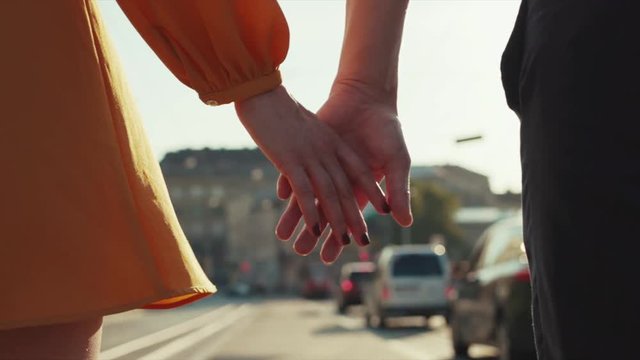 Low angle shot of male and woman hands holding together, walking in the city on the bright sunlight. Dating, romantic relationships, romantic atmosphere. Love story
