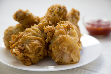 Fried chicken drumsticks on white plate with sauce, side view. Close-up.