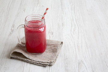Glass jar of watermelon smoothie on a white wooden table, side view. Copy space and text area.