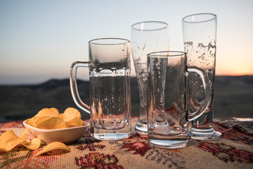Close up empty mugs of beer on a sunrise background with mountains. Beer party is over concept.