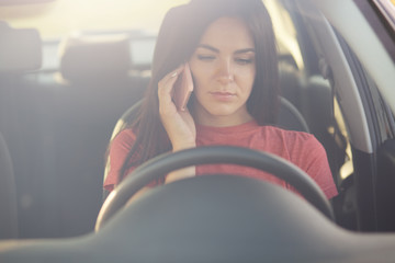 Serious beautiful female talks via cell phone with husband, doesn`t know what to do as stops on road, has no petrol in automobile, asks for help, has dark hair, rides for work. People, driving concept
