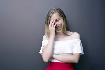 Blonde young woman covering face with hand and looking at camera