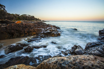 Moving waves breaking over rocky shore at sunrise