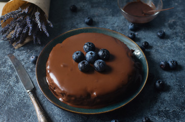Homemade blueberry cheesecake with chocolate topping and fresh organic berries, lavender on a dark stone background. Selective focus