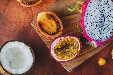 Raw fresh exotic fruits on wooden board and dark background. Healthy lifestyle, organic food. Dragon fruit, passionfruit, tamarillo, coconut, physalis, top view, selective focus