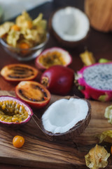 Raw fresh exotic fruits on wooden board and dark background. Healthy lifestyle, organic food. Dragon fruit, passionfruit, tamarillo, coconut, physalis, selective focus