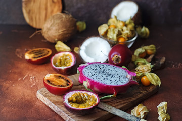 Raw fresh exotic fruits on wooden board and dark background. Healthy lifestyle, organic food. Dragon fruit, passionfruit, tamarillo, coconut, physalis, selective focus