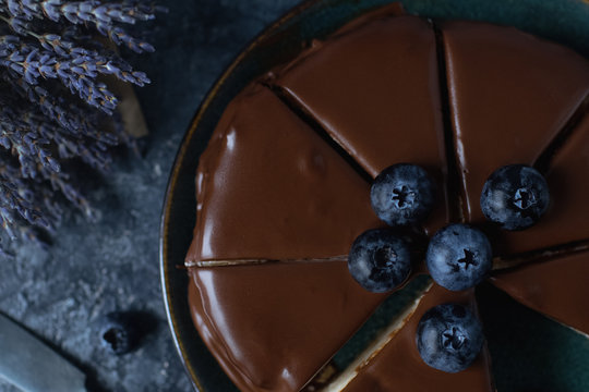 Homemade blueberry cheesecake with chocolate topping and fresh organic berries, lavender on a dark stone background. Selective focus, top view