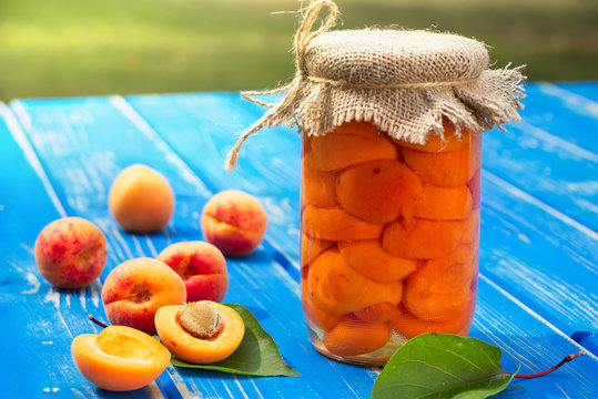 Homemade tasty apricot compote in glass jar and apricot fruit on blue wooden table