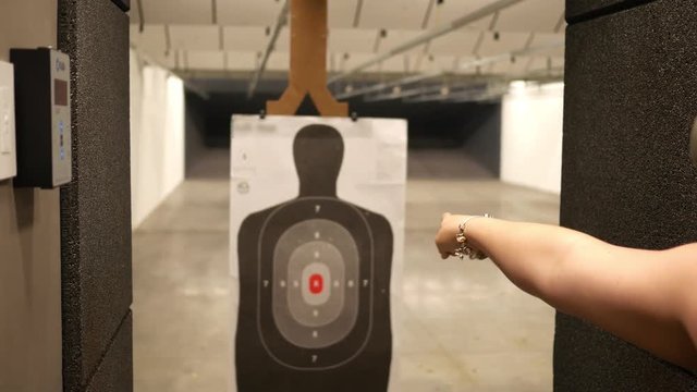 Woman uses a motorized slider to move a target closer at a indoor firing range