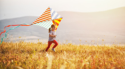 happy child girl running with kite at sunset outdoors.