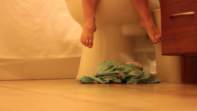 Little feet hanging down on the toilet, with pajamas that fall to the floor.
