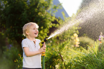 Funny little boy playing with garden hose in sunny backyard