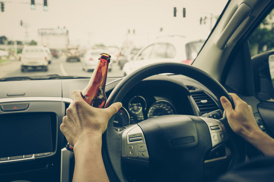 A driver holding alcoholic bottle while driving / Drunk driving concept