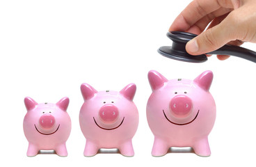 Hand holding a stethoscope over smiling pink piggy banks isolated on white