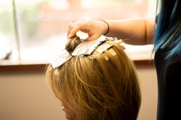 Fototapeta premium Blonde woman receiving haircut at a salon. Woman with blonde highlights. Hair foils on a female client. Master stylist cutting hair