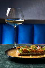 Smorrebrod Danish sandwich with salmon fish, curd mousse, marinated cucumber and radish. Delicious vegetarian snack food with dark rye bread and different topping and wine glass at restaurant table
