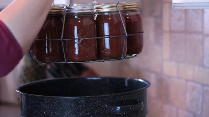 A rack of glass jars or bottles is pulled out of the pot of hot water.