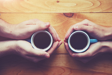 Fototapeta na wymiar Hands of couple with two cups of morning coffee on wooden table. View from above
