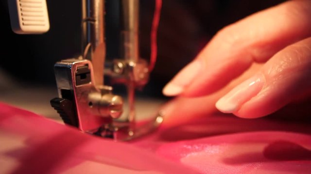 Woman's hands move some pink material into a sewing machine.