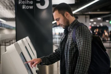 Deurstickers Young man with backpack touching interactive display using self service machine, doing self-check-in for flight or buying airplane tickets at automatic device in modern airport terminal building © romankosolapov