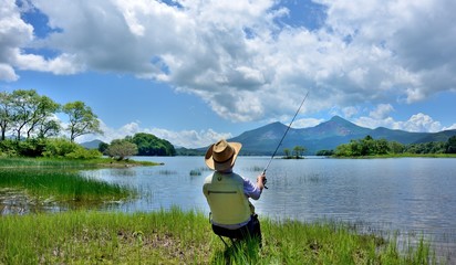 夏の湖畔・のんびりと釣りをする男性