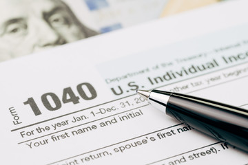 Tax time concept, selective focus on pen on 1040 US individual income tax filling form with US dollar bill, calculate from yearly revenue to pay the government