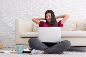 Asian woman freelance raise arm and rest at back of head and close eye in front of laptop computer in living room at home,relax from hard work.work at home.