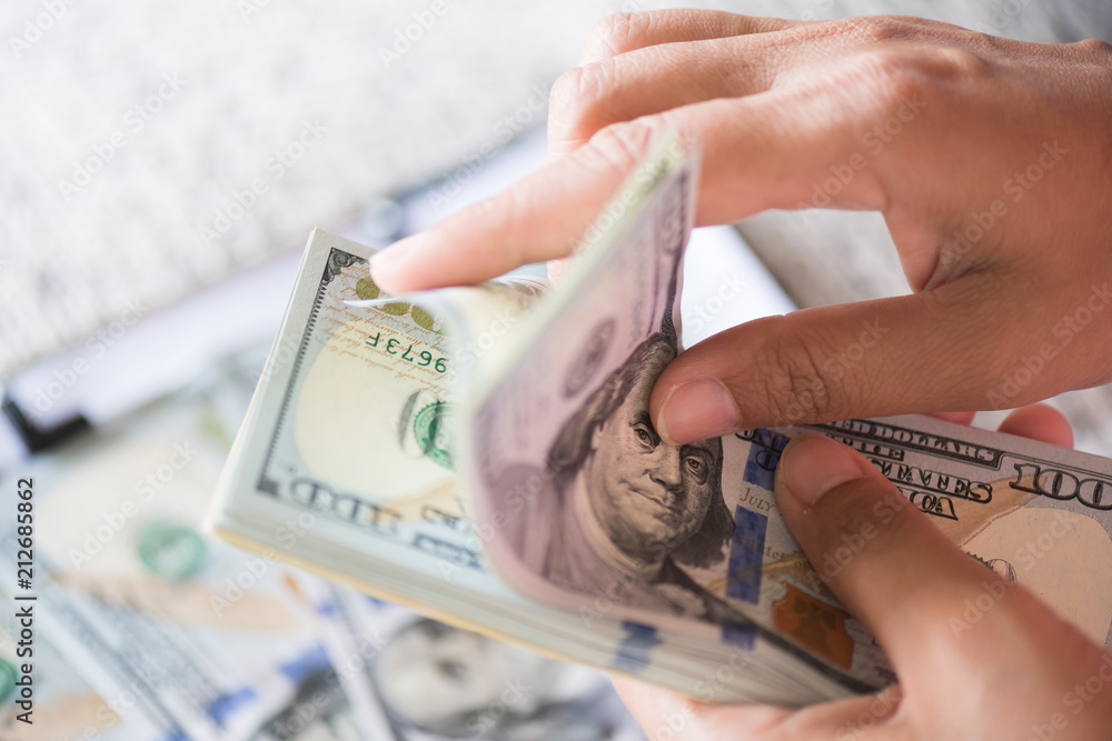 Wall mural Close up woman hands holding and counting bunch of America dollars banknotes calculator and red pencil in background.