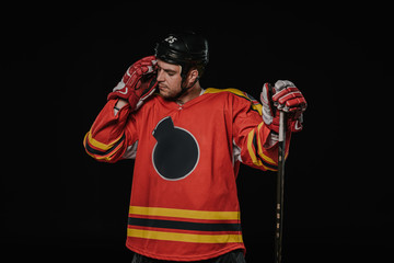 tired hockey player standing with hockey stick isolated on black