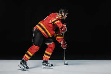 side view of young professional sportsman playing ice hockey on black