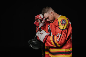 side view of hockey player holding helmet and leaning at hockey stick isolated on black - Powered by Adobe