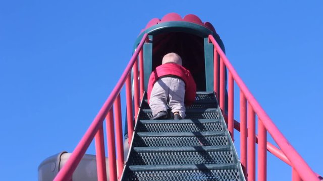 Little boy climbing park slide stairs.