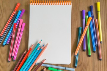 bright multicolored pencils and markers next to a sketchbook on a wooden table