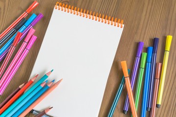 bright multicolored pencils and markers next to a sketchbook on a wooden table