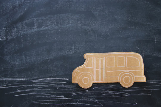 Back to school concept. Top view image cardboard school bus over classroom blackboard background.