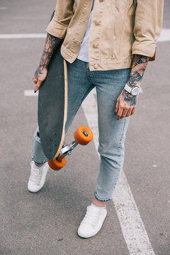 cropped image of stylish tattooed woman holding skateboard at parking lot
